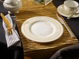 Ivoire sur une table Un couvert avec assiette, couteau, fourchette, tasse, sous-tasse et serviette sur un chemin de table à la structure dorée.