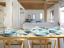 Une table à manger dressée avec de la vaisselle et des verres Aqua bleu nacré dans un salon lumineux, moderne et ouvert avec des poutres apparentes.