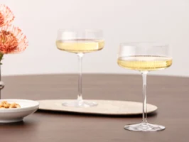 Deux verres Afina remplis de vin pétillant sur une table en bois Deux verres Afina remplis de vin pétillant sur une table en bois, à côté de fleurs et d'un petit bol.