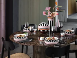 Memphis de Villeroy & Boch élégamment décoré Une table ronde en marbre avec quatre couverts, de la vaisselle Memphis rayée, des verres à vin et un vase avec des fleurs roses