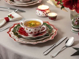 Une table de fête dressée avec une tasse à soupe et plusieurs assiettes Une table de fête dressée avec une tasse de soupe, des assiettes empilées, des couverts, des bougies et des décorations festives.