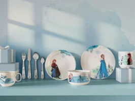 Vaisselle et ustensiles pour enfants à l'effigie des personnages de La Reine des neiges, présentés dans des coffrets cadeaux bleus sur une étagère bleue.