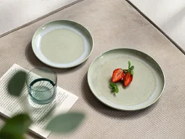 Vue rapprochée d’une table avec des assiettes vert tendre Perlemor Alga de Villeroy & Boch, décorées d’une figue coupée en deux pour une touche naturelle. Le service est complété par un verre à eau Like Sage, créant une atmosphère calme et raffinée où formes organiques et tons terreux s’unissent en parfaite harmonie.