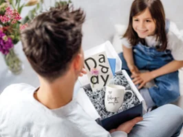Une tasse à café « Lieblingsmensch » (Personne préférée) offerte comme cadeau dans un salon Une jeune fille remet à son père, dans le salon, une boîte cadeau contenant une tasse à café portant l’inscription « Lieblingsmensch » (Personne préférée).