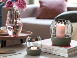 Deux photophores Rose Garden de Villeroy & Boch sont posés sur une pile de livres. Deux photophores Rose Garden de Villeroy & Boch sont posés sur une pile de livres à côté d'un vase rose Rose Garden avec des fleurs, le tout sur une table ronde dans une ambiance de salon confortable.
