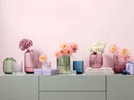 Vases en verre Fleur de différentes couleurs pastel et tailles Différents vases en verre aux couleurs pastel de la collection Fleur, décorés de fleurs, sont disposés sur une surface claire avec des livres et de petits objets décoratifs devant un mur rose.