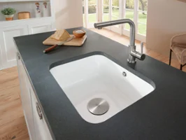 Un évier Cisterna encastré dans un plan de travail anthracite Un évier sous plan Cisterna blanc est encastré dans un plan de travail anthracite. Une planche de bois avec un couteau est posée dessus
