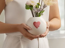 Vase rond « with love » avec motif cœur rouge Femme tenant un vase rond blanc « with love » avec un cœur rouge-rose et des fleurs blanches.