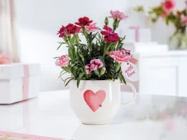 Une tasse blanche With Love avec un cœur rouge Une tasse With Love blanche avec un cœur rouge et des fleurs roses et rouges est posée sur une table blanche.