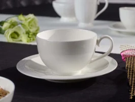 Une tasse White Pearl avec sous-tasse Une tasse et sous-tasse blanches en porcelaine sur une nappe noire, avec des tasses blanches floues en arrière-plan et une fleur décorative.