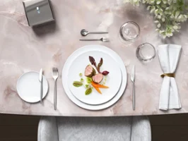 De la vaisselle et des couverts de table MetroChic sur une élégante table en marbre Une table élégante en marbre avec un plat gourmand servi dans des assiettes blanches MetroChic, accompagné de couverts de table MetroChic et d’une décoration florale.