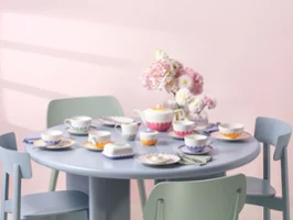 Une table ronde bleu pastel avec un service à thé fleuri composé de tasses à thé colorées, de petits bols, d'assiettes et d'une théière de la collection Fleur.