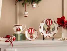 Annual Chistmas edition 2026 collection Des assiettes, tasses et bols en céramique festifs avec des motifs de montgolfières rouges de Villeroy & Boch sont présentés avec des fleurs rouges et des décorations de Noël.