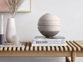 La Boule Pure Beige sur une table en bois La Boule beige de Villeroy & Boch sur une table en bois à côté d’une Manufacture vase et de livres.