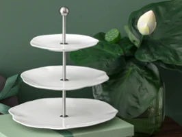 Étagère Pura blanche à trois niveaux avec poignée métallique à côté d'une plante de lotus Étagère Pura blanche à trois niveaux avec poignée métallique, à côté d'un grand lotus vert et d'un coffret cadeau fermé.