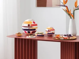 La Boule and La Petite Boule, a white Manufacture Collier blanc vase Intérieur moderne avec La Boule et La Petite Boule, un vase blanc Manufacture Collier blanc avec des fleurs orange, et une œuvre murale abstraite aux tons doux.