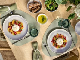 Deux assiettes Perlemor beiges avec salade et fromage burrata Deux assiettes de salade au fromage burrata, servies avec du pain, de la salade verte et un bol d'huile d'olive sur une table à manger.