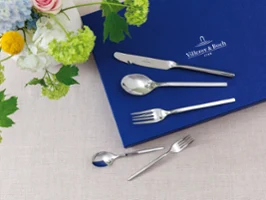 Set de couverts avec couteau, cuillère et fourchette sur un tissu bleu à côté d'une composition florale sur fond beige Set de couverts avec couteau, cuillère et fourchette sur un tissu bleu à côté d'une composition florale sur fond beige