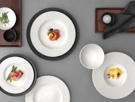 A formal table setting with Manufacture plates A formal table setting with a white and black plates, with food on it on a grey table.