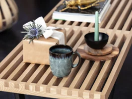 Un mug Lave et une boîte cadeau sur un plateau en bois Un mug Lave, une boîte cadeau avec un ruban et plat creux sur un plateau en bois, sur une table élégante.