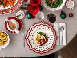 A festively laid table Une table dressée pour les fêtes avec des assiettes décorées, des verres à vin et un centre de table composé de fleurs rouges et d'ornements.