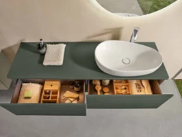 Une console de salle de bains Antao verte avec lavabo Une console d’un vert naturel dans la salle de bains avec deux tiroirs ouverts et remplis, surmontée d’une vasque blanche Antao de Villeroy & Boch.