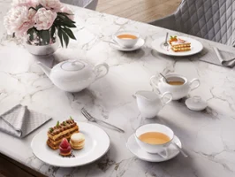 Un service à thé Anmut élégant et gracieux sur une table en marbre Un élégant service à thé Anmut sur une table en marbre, composé d’une théière, de tasses et d’un pot à lait avec du thé et des biscuits.