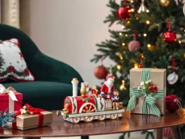 Une locomotive Christmas Toys Memory sur une table en bois Un sapin de Noël décoré, des cadeaux et une locomotive Christmas Toys Memory sur une table en bois à côté d'une chaise verte.