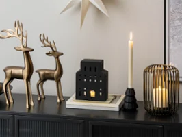 Deux rennes en métal, des bougeoirs et une lanterne noire en forme de maison posés sur un buffet noir.