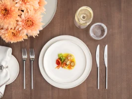 Une petite entrée, du vin et de l'eau seront servis sur une table soigneusement dressée, avec des assiettes Afina et des couverts en argent.