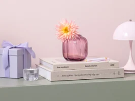 Petit vase en verre Fleur sur une étagère verte Le petit vase en verre rose de Fleur avec une fleur est posé sur des livres empilés sur une étagère vert pastel.