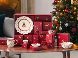 Une table avec un calendrier de l'Avent et de la vaisselle festive de Villeroy & Boch à côté d'un sapin de Noël décoré dans un salon confortable.