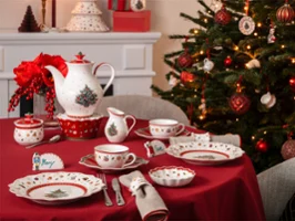 A table set with crockery and cutlery Une table dressée avec de la vaisselle et des couverts aux motifs de Noël, à côté d'un sapin de Noël décoré et d'une cheminée illuminée.