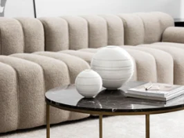 Sur une table basse en marbre noir trône La Boule en différentes tailles Un salon moderne avec un canapé gris texturé et une table basse en marbre noir décorée avec La Boule en différentes tailles.