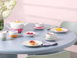 Un service à thé avec des pièces de vaisselle Fleur colorées sur une table ronde bleu clair Un service à thé aux couleurs pastel avec des tasses, des soucoupes, des assiettes aux motifs floraux colorés de la collection Fleur et des petits desserts sur une table ronde bleu clair.
