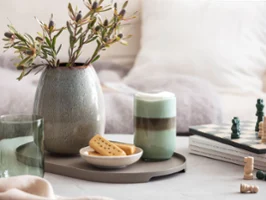 Une verre Like Sage avec du café et un vase Lave Home Un verre Like Sage avec du café, un échiquier, des biscuits et un vase Lave avec de l’herbe de la pampa sur un plateau de table.