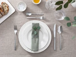Assiettes blanches Manufacture sur une table avec des feuilles d’eucalyptus Une table dressée avec des assiettes Manufacture blanches de Villeroy & Boch ainsi que des feuilles d’eucalyptus et des couverts de table.