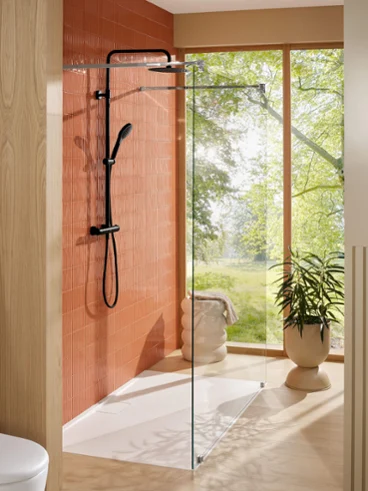 Douche moderne avec parois en verre et robinetterie noire, à côté d’une grande fenêtre donnant sur la verdure.