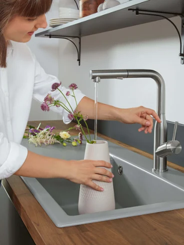 Au-dessus d’un évier de cuisine Subway Style, une femme remplit un vase à l’aide d’une robinetterie de cuisine Subway Style.