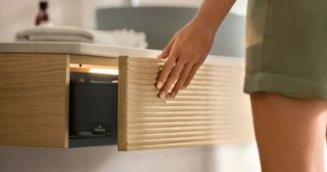 Une console minimaliste Antao pour la salle de bains Dans une salle de bains, une femme ouvre un tiroir de console de la collection de meubles de salle de bains Antao de Villeroy & Boch.