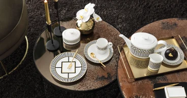 Un service à thé MetroChic sur une table ronde avec notes dorées, accompagné d’orchidées, de bougies et de petits snacks.