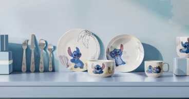Une série d'assiettes et de tasses de la collection Disney Stitch sont disposées sur une étagère bleu clair. Une série d'assiettes et de tasses de la collection Disney Stitch sont décorées de motifs de dessins animés et exposées sur une étagère bleu clair avec des ustensiles.