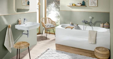 Une baignoire O.novo blanche dans une salle de bains moderne vert clair Une salle de bains avec des murs verts, des meubles en bois et une baignoire blanche ainsi qu’un lavabo blancs O.novo.