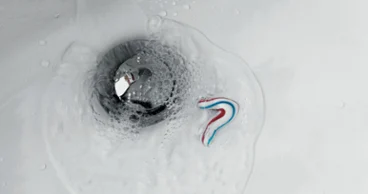 Une petite quantité de dentifrice et d’eau s’écoule via l’évacuation d’un lavabo de salle de bains, formant des bulles autour du cache-bonde.