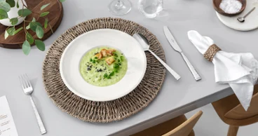 Des couverts de table Blacksmith et des assiettes Artesano de Villeroy & Boch, accompagnés d’une décoration rustique et de vin blanc Une table dressée pour le repas avec des couverts de table Blacksmith, une assiette Artesano remplie de soupe, un verre à vin blanc et une décoration de table rustique.