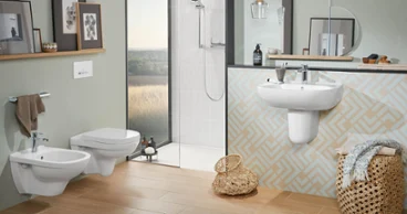 La salle de bains moderne avec des carreaux beiges et des murs pastel est équipée de WC suspendus O.novo, d’un bidet, d’un lavabo avec miroir et d’une douche à l’italienne. Les étagères sont garnies d’œuvres d’art encadrées et d’articles de toilette. Des paniers sont posés sur le sol.
