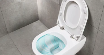 Des toilettes murales avec technologie Flush de Villeroy & Boch, sur fond de carrelage gris. Le couvercle des toilettes est ouvert et laisse entrevoir la cuvette qui contient une solution de nettoyage.