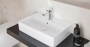 Lavabo simple Minimalist Memento 2.0 en blanc brillant, posé sur un plan de travail foncé avec un robinet chromé moderne pour un look de salle de bain élégant.