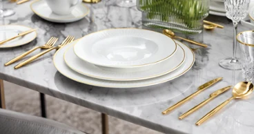 De la vaisselle Château Septfontaines avec MetroChic d’Or sur une table en marbre Une décoration de table élégante avec des assiettes blanches Château Septfontaines, des couverts de table dorés MetroChic d’Or et des verres en cristallin sur une table en marbre.
