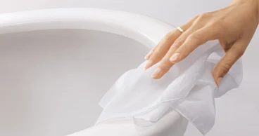 Une main portant une bague essuie des WC en céramique blanche avec un chiffon blanc.